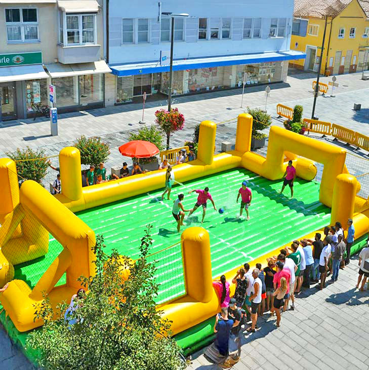 Kinder und Erwachsene spielen Water Soccer beziehungsweise Soap Soccer in einem zum mieten, aufblasbaren Fussbalfeld