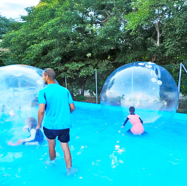 Wasserbecken mit Kinder in Wasserbaellen und ein Mann der das bewacht.
