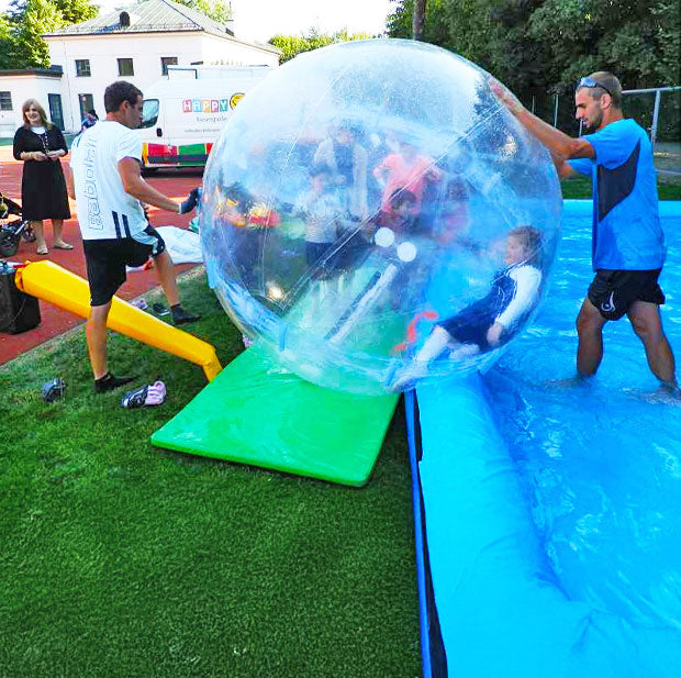 2 Maenner mit einem Kind in einem aufblasbarem Wasserball am Beckenrand
