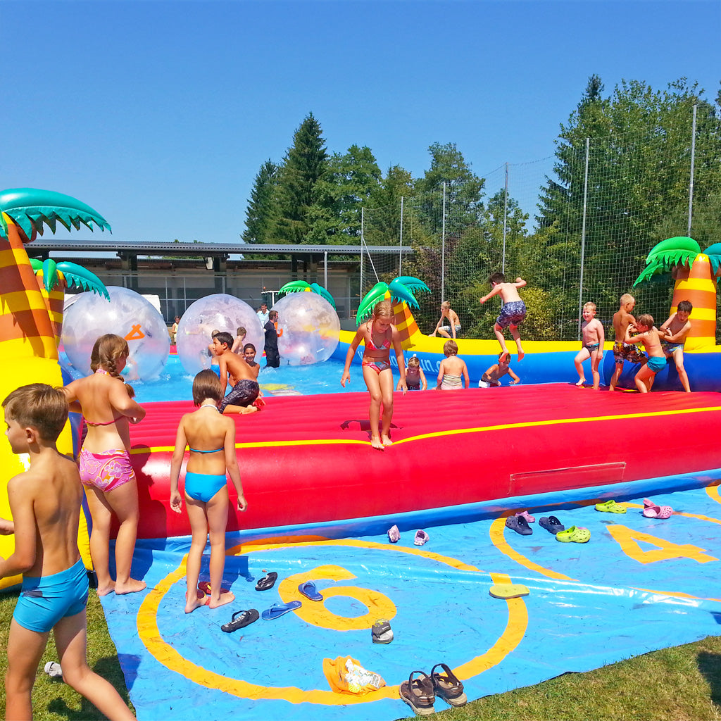 Aufblasbares Water Run Becken mit vielen Kindern die plantschen und über das Wasser laufen.