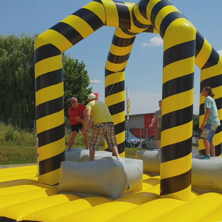 Kinder und Erwachsene stehen auf Podesten in einer aufblasbaren Arena und versuchen, sich mit einer großen schwingenden Abrissbirne gegenseitig aus dem Gleichgewicht zu bringen – ein actionreiches Gruppenspiel mit Spaßgarantie.