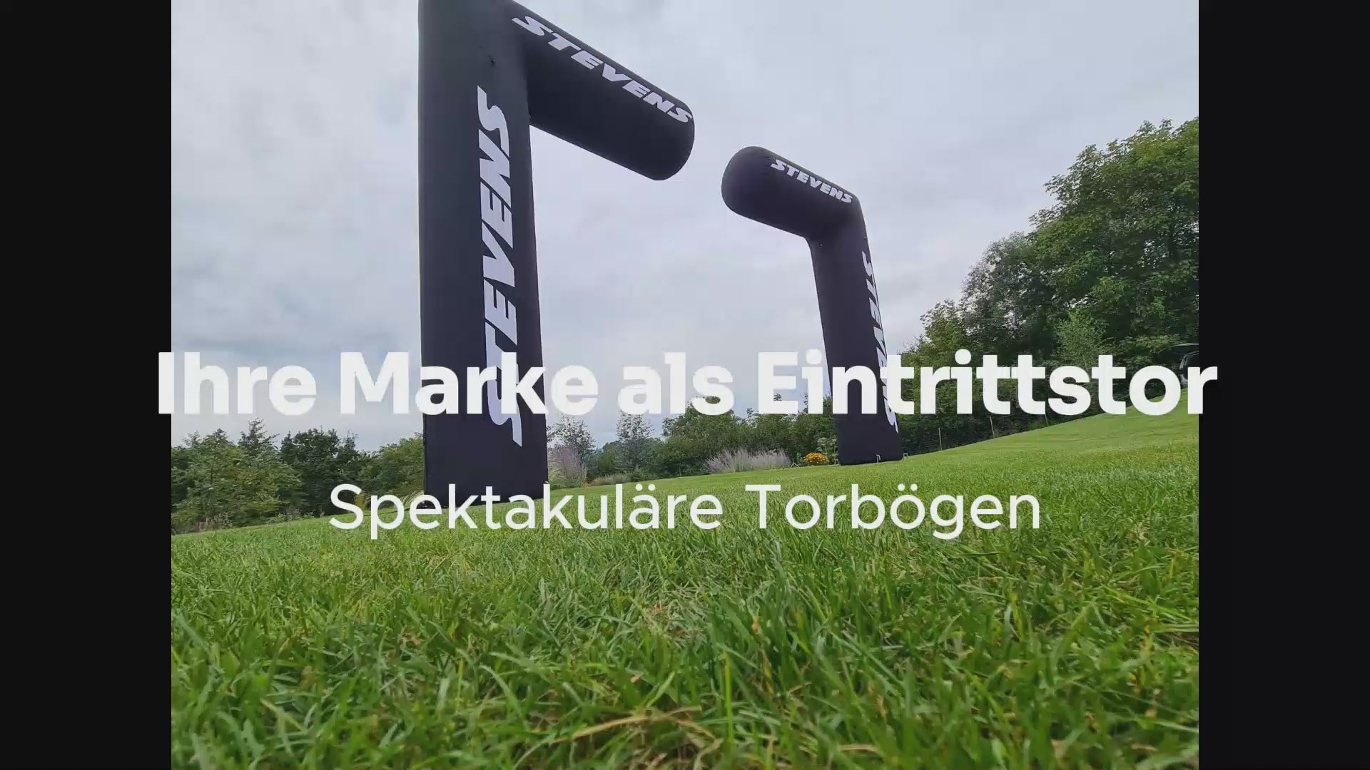 Individueller aufblasbarer Werbebogen in kräftigen Farben markiert den Start- oder Eingangsbereich einer Veranstaltung, Wind sorgt für sanfte Bewegungen des stabil verankerten Bogens.