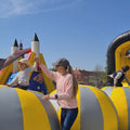 Kinder balancieren über aufblasbare Kugeln auf einer schwarz-gelben Hüpfburg, Geschicklichkeit und Schnelligkeit sind gefragt, um nicht zu stürzen.