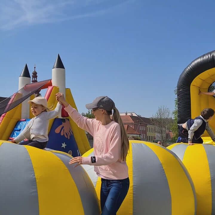 Kinder balancieren über aufblasbare Kugeln auf einer schwarz-gelben Hüpfburg, Geschicklichkeit und Schnelligkeit sind gefragt, um nicht zu stürzen.