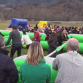 Teilnehmer sind an Stangen fixiert und bewegen sich wie bei einem Riesenwuzzler Tischfußballspiel, während sie versuchen, gemeinsam Tore zu erzielen – Teamwork und Spaß stehen im Mittelpunkt.
